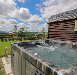 An outdoor hot tub with water flowing next to a wooden building under a partly cloudy sky at Woodland View in Rhayader