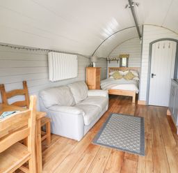 A small living area with a wooden dining table and chairs a white sofa a wooden bed chest of drawers and a kitchen area in a pod style room at Woodland View in Rhayader