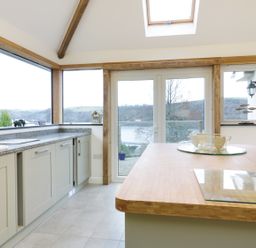 A kitchen with cabinets and a wooden countertop next to large windows and glass doors at Treetops Golant near Fowey