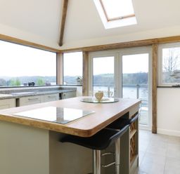 A kitchen with an island and bar stools overlooking a river through large windows at Treetops in Golant near Fowey