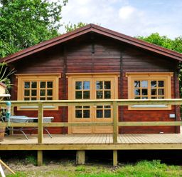 A wooden cabin with a deck and railing in a garden with trees and a birdhouse at St Hildas Lodge in Hinderwell near Runswick Bay