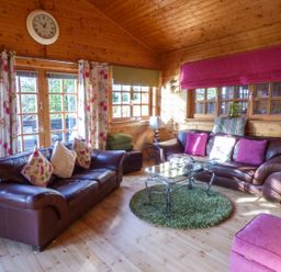 A wooden living room with two brown leather sofas pink and floral cushions glass coffee table and floral curtains at St Hilda's Lodge in Hinderwell near Runswick Bay