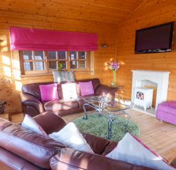 A wooden living room with brown leather sofas pink cushions a glass coffee table and a wall-mounted TV at St Hildas Lodge in Hinderwell near Runswick Bay