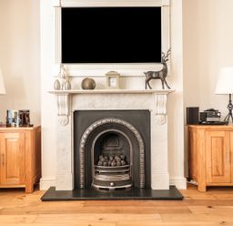A fireplace with a white mantle and firewood surrounded by two wooden cabinets each with a lamp on top at 33 Crescent Gardens in Bath