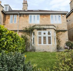 Front view of a two-story stone house with multiple windows and a small garden with green shrubs and grass at 33 Crescent Gardens in Bath