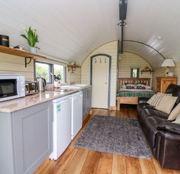 A compact living space with a kitchen area featuring appliances and shelves a sofa a rug and a bed in the background at Mountain View in Rhayader