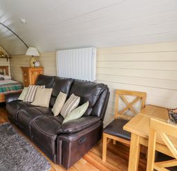 A living area with a brown leather sofa and cushions a wooden dining table with chairs a bed with pillows and a blanket and a wooden dresser with a lamp at Mountain View in Rhayader