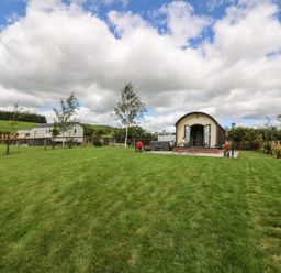 A small cabin with a patio and chairs on a grassy lawn surrounded by a fence and trees at Mountain View in Rhayader