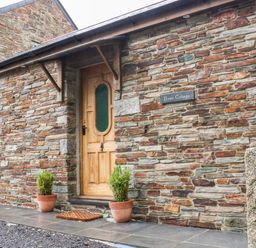 The entrance of a stone cottage with a wooden door two potted plants a doormat and a sign saying Elvan Cottage in Liskeard