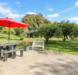 A patio with a picnic table and red umbrella a white bench and a rotary clothesline in a garden at Beehive Cottage Kilbrittain County Cork