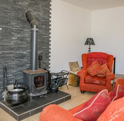 A living room with a wood-burning stove and red armchairs at Beehive Cottage in Kilbrittain County Cork
