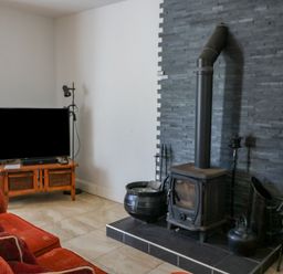 A living room with a red sofa a television on a wooden stand and a wood-burning stove on a tiled hearth at Beehive Cottage in Kilbrittain County Cork
