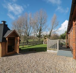An outdoor space with a wooden cabin with chimney a gravel area a wooden deck and trees in the background at Sunnyside Lodge in Crewkerne