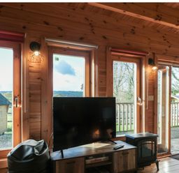 A wooden room with large windows a television on a cabinet a beanbag chair and a small stove at Sunnyside Lodge in Crewkerne