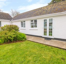 A white exterior wall with windows and a glass door next to a garden with grass and bushes at 4 Hanbury Lodge in Pentlepoir