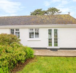 A white exterior wall with two windows and glass double doors next to a garden with shrubs at 4 Hanbury Lodge in Pentlepoir