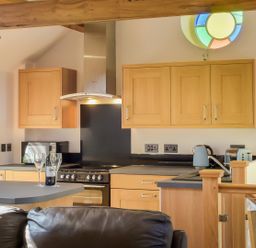 A kitchen with wooden cabinets a black countertop a stove a kettle and a bottle with glasses on the counter at Moor View Chapel in Camelford