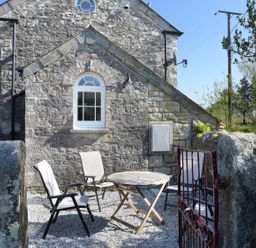 An outdoor seating area with four chairs and a round table on gravel outside a stone building at Moor View Chapel in Camelford
