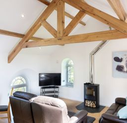 A living room with leather sofas a wood stove a television and wooden beams at Moor View Chapel in Camelford