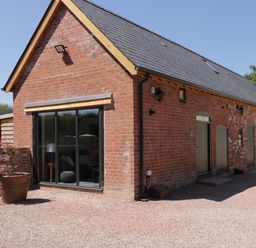 A brick building with a sloped roof and large sliding glass door at The Stables in Cross Keys near Hereford