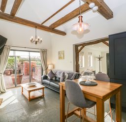 A living and dining area with a black sofa wooden dining table chairs and exposed wooden beams at The Stables in Cross Keys near Hereford
