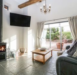 A living room with a wood burning stove television coffee table and leather sofa at The Stables in Cross Keys near Hereford