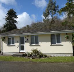 A single story house with a white door and three windows surrounded by trees at Little Retreat in Liskeard