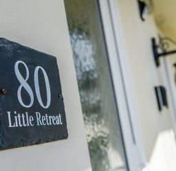 A close up of a house number sign 80 Little Retreat on a wall with a door and lantern in Liskeard