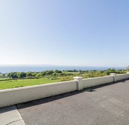 A paved outdoor area with a low wall overlooking green fields and a large body of water at Tullyally in Redcastle