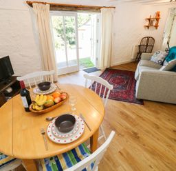 A dining area with a wooden table set for two and a living space with a sofa and a red rug near glass doors at The Granary Cottage in Llangrannog near Cardigan