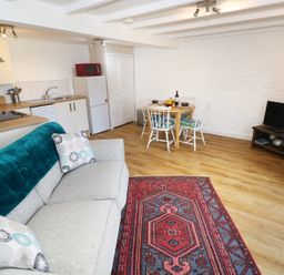 A living room with a grey couch, patterned rug, dining table with chairs, kitchen area, and a television at The Granary Cottage in Llangrannog near Cardigan
