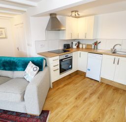 A kitchen area with white cabinets and wooden countertop next to a grey sofa with cushions at The Granary Cottage in Llangrannog near Cardigan