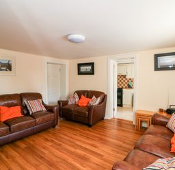 A living room with three brown leather sofas with colorful pillows and wooden flooring at Grange Farmhouse in Fethard-on-Sea County Wexford