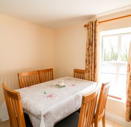 A dining room with a wooden table covered by a floral tablecloth and surrounded by wooden chairs near a window with patterned curtains at Grange Farmhouse in Fethard-on-Sea County Wexford