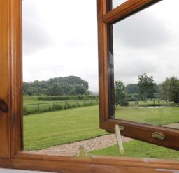 A view of a garden with grass trees and a path visible through a wooden framed open window at The Old Goat Barn at Trout Cottage Somerton