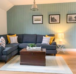 A living room with a dark corner sofa with cushions and a wooden chest coffee table on a rug at Oh Buoy in Charlestown