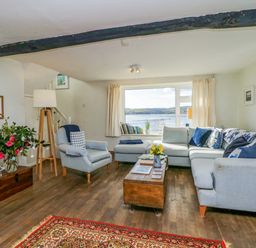 A living room with a sectional sofa armchair wooden coffee table flowers and a view of the water at Clamoak Cottage in Clamoak near Bere Alston