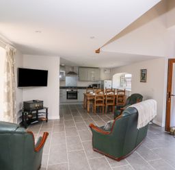 An open plan living room with green leather armchairs a dining table and chairs and a kitchen with grey cabinets at Cilgwyn Bach in Llandysul