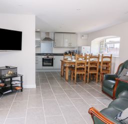 A kitchen and dining area with a wooden table and chairs a green leather sofa and armchair and a wall-mounted television at Cilgwyn Bach in Llandysul