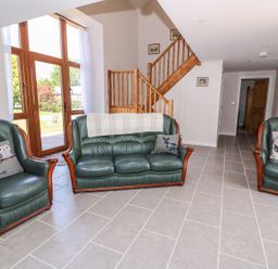 A living room with green leather sofa and chairs next to wooden staircase at Cilgwyn Bach in Llandysul
