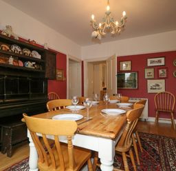 A dining room with wooden table set with plates and glasses wooden chairs and a decorated cabinet against a red wall at Dale House in Lorton