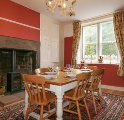 A dining room with a wooden table set for six next to a fireplace and a window with floral curtains at Dale House in Lorton