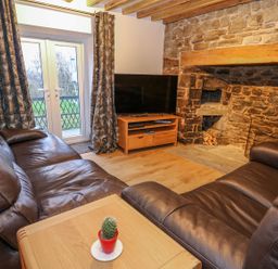 A living room with leather sofas a wooden table with a small plant a stone fireplace and a TV on a stand at Crooked Hill Cottage in Ammanford