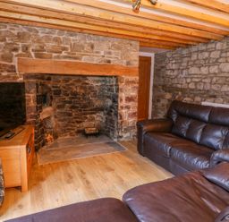A living room with stone walls wooden beams a stone fireplace brown leather sofas and a wooden TV stand at Crooked Hill Cottage in Ammanford