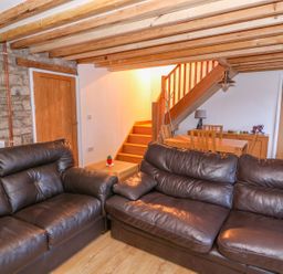A living room with two brown leather sofas a wooden dining table under stairs and wooden beams on the ceiling at Crooked Hill Cottage in Ammanford