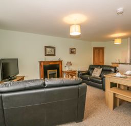 A living room with black leather sofas a wooden dining table and chairs a television and a fireplace at 2 Park Nook Close in Waberthwaite