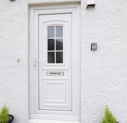 A white front door with a window and sign reading Park Nook Close on a textured white wall with two small plants in pots on either side at 1 Park Nook Close in Waberthwaite