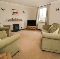 A living room with three green upholstered chairs a television on a wooden stand a window and wall-mounted lights at 1 Park Nook Close in Waberthwaite