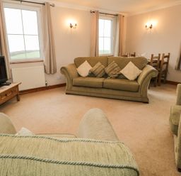 A living room with green sofas a wooden TV stand with a television and a dining area at 1 Park Nook Close in Waberthwaite