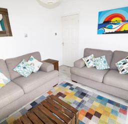 A living room with two gray sofas and patterned cushions a wooden coffee table a colorful rug a wooden framed mirror and a colorful wall painting at Driftwood in Bude